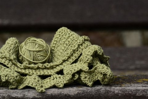 Ein gr&uuml;nes Wollkn&auml;uel , welches zur H&auml;lfte schon verh&auml;kelt ist, das Geh&auml;kelte liegt unter dem Wollkn&auml;uel